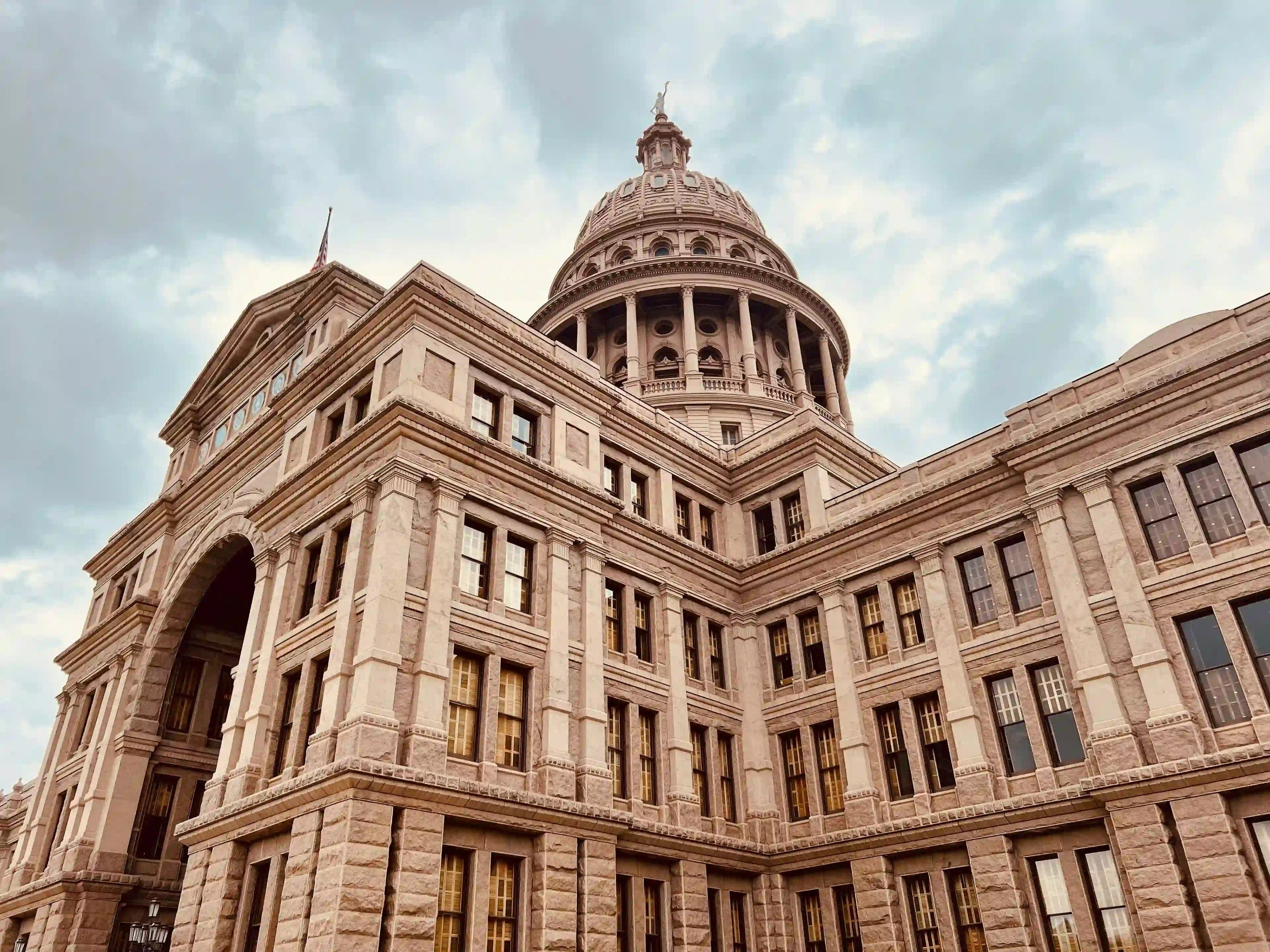 Looking up at the Texas State Capitol, an Italian Renaissance Revival–style building with a prominent columned dome centered around the three story structure.