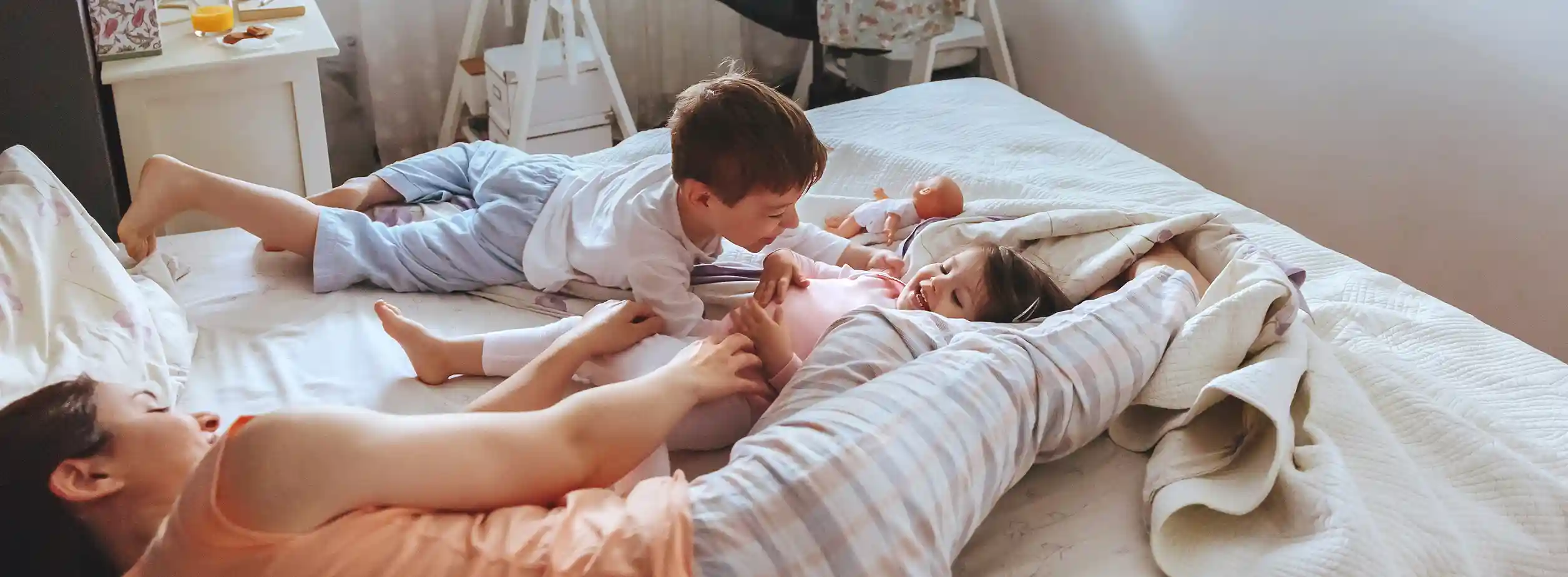 A light skinned mother and her two children enjoy a lazy day laying in bed.